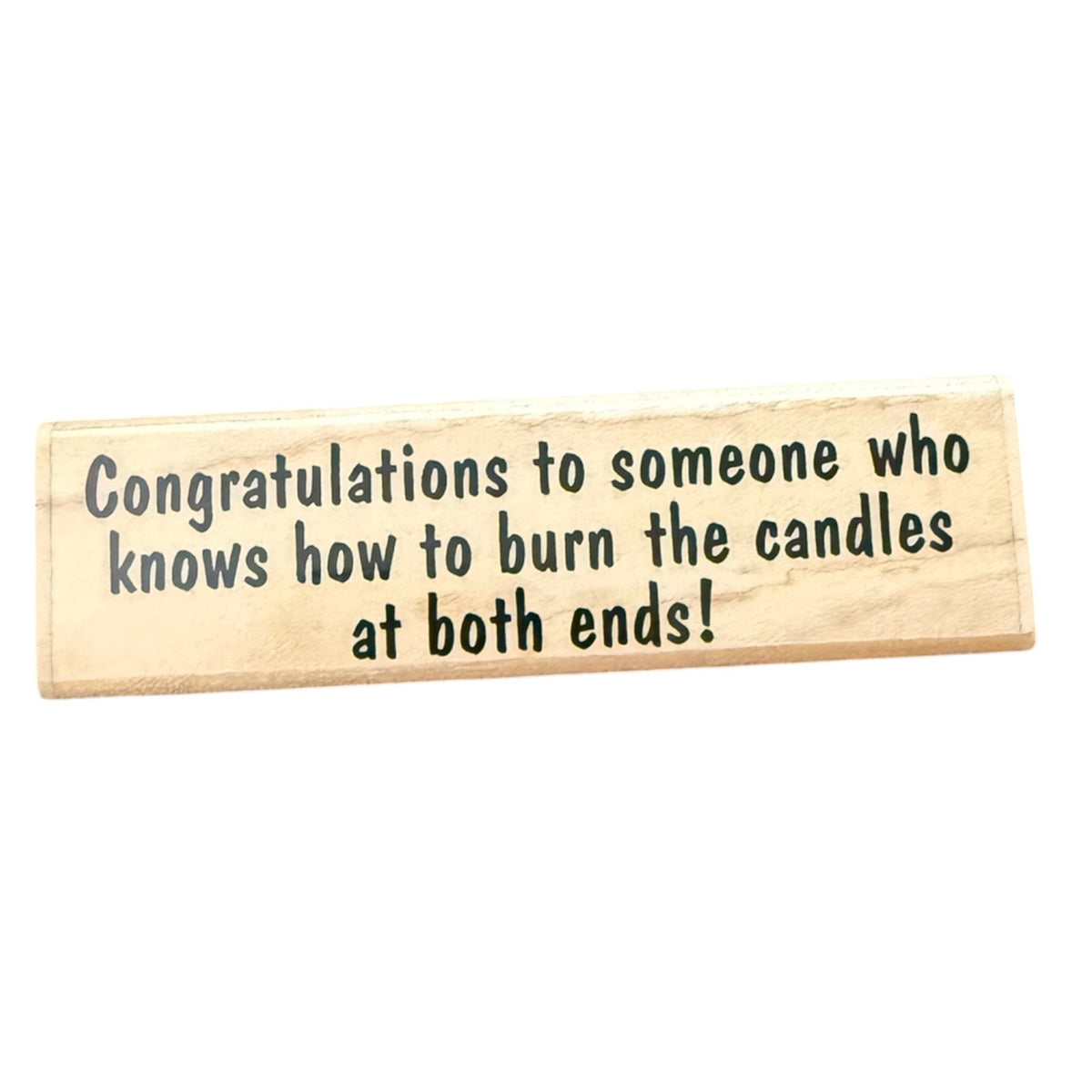 A rectangular light wood rubber stamp with black printed text that reads, 'Congratulations to someone who knows how to burn the candles at both ends!' on a plain white background.