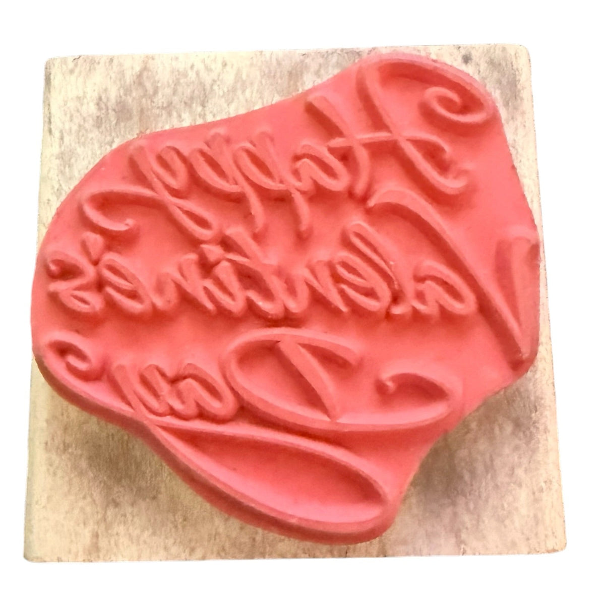 A pink rubber stamp with the words 'Happy Valentine's Day' in cursive, mounted on a square light wood block against a white background.
