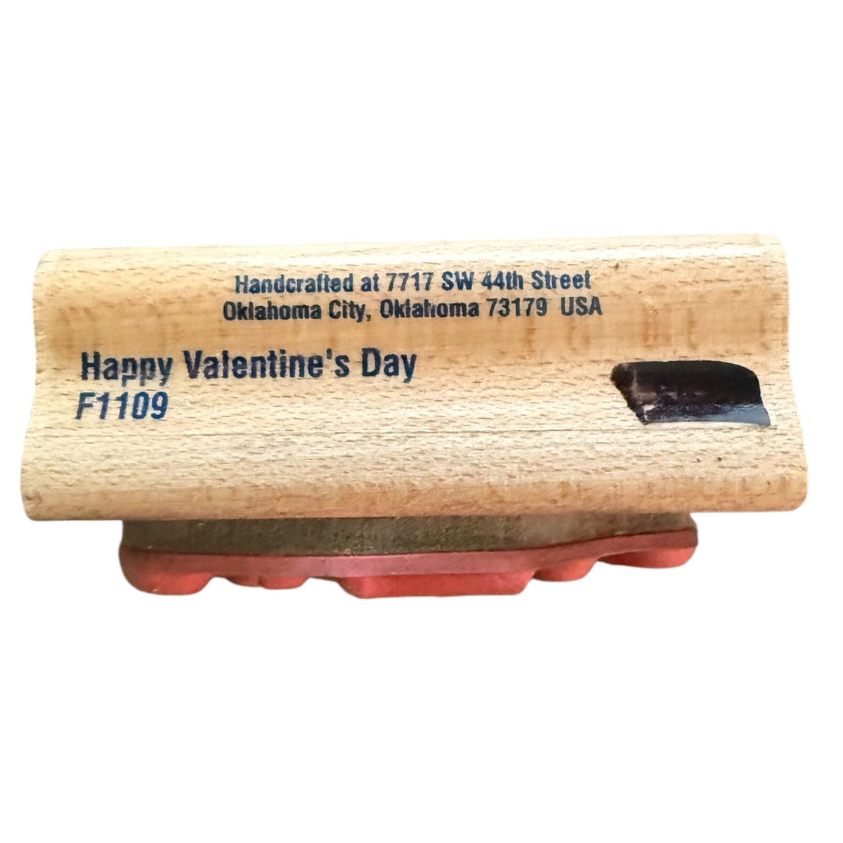 A wooden stamp block with a rubber stamping surface, featuring the text 'Happy Valentine's Day F1109' and 'Handcrafted at 7717 SW 44th Street, Oklahoma City, Oklahoma 73179 USA' printed on the side.