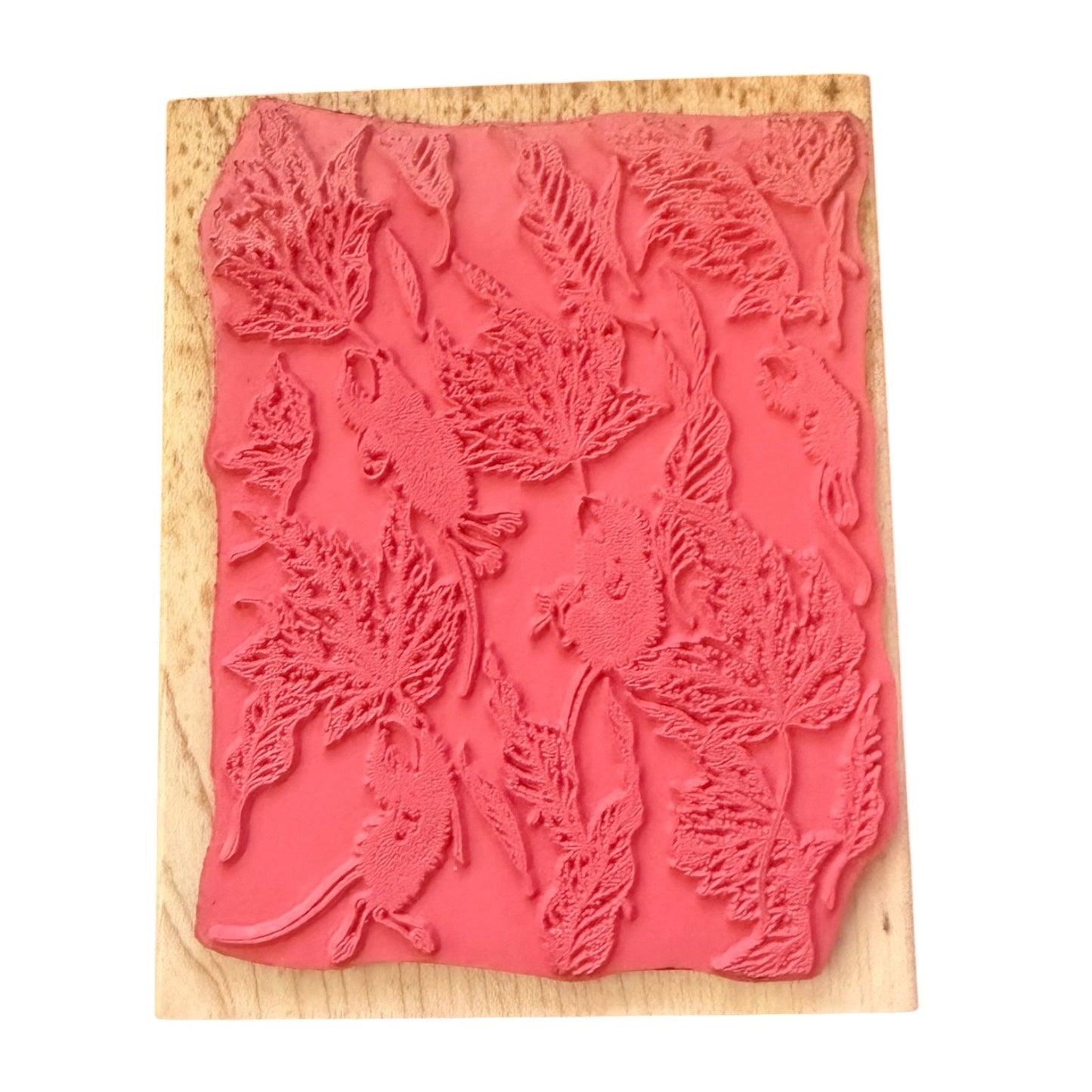 A pink rubber stamp with an embossed pattern of leaves and small mice, mounted on a light-colored wooden block against a plain white background.