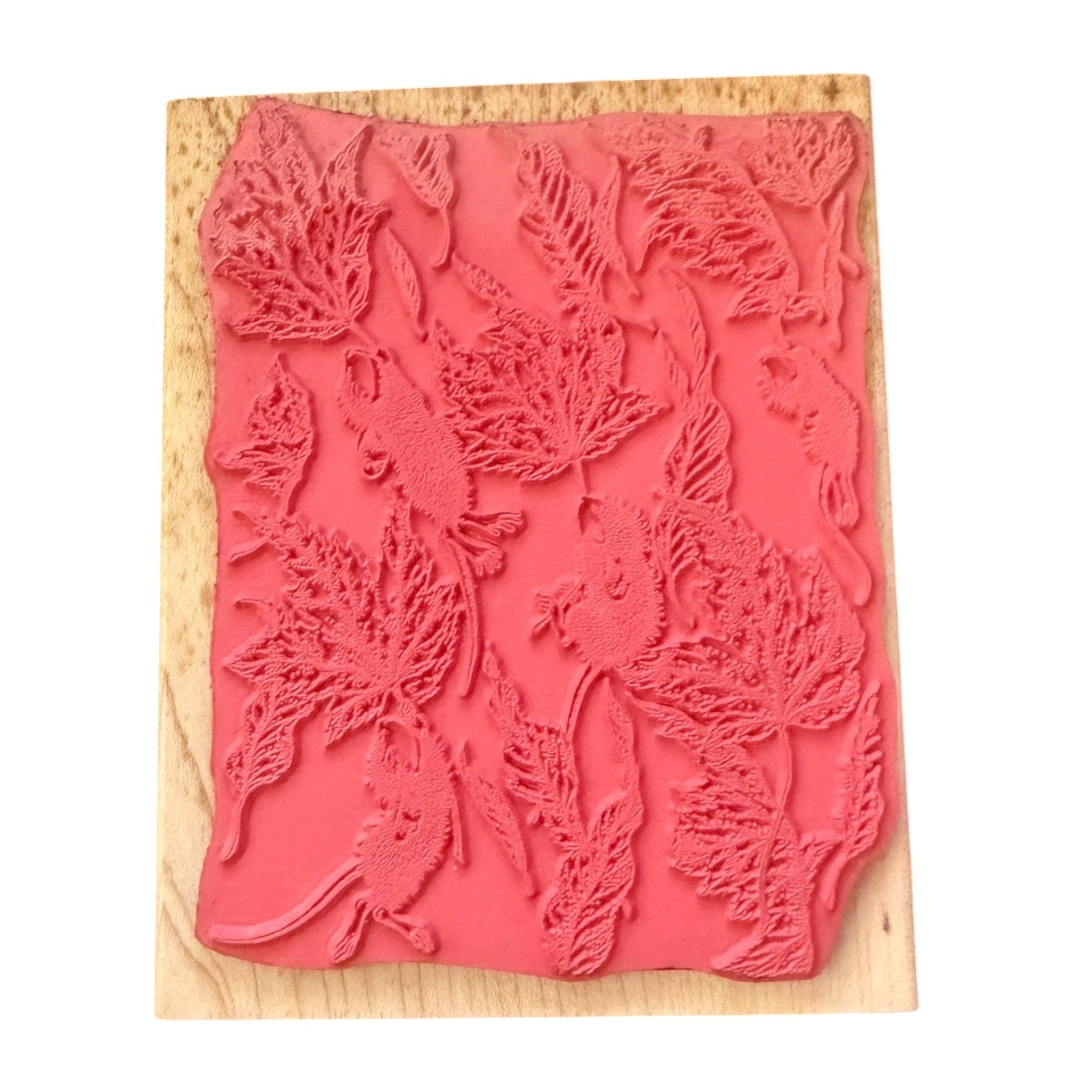 A pink rubber stamp with an embossed pattern of leaves and small mice, mounted on a light-colored wooden block against a plain white background.