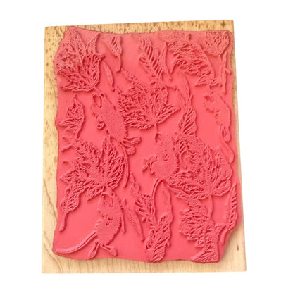 A pink rubber stamp with an embossed pattern of leaves and small mice, mounted on a light-colored wooden block against a plain white background.