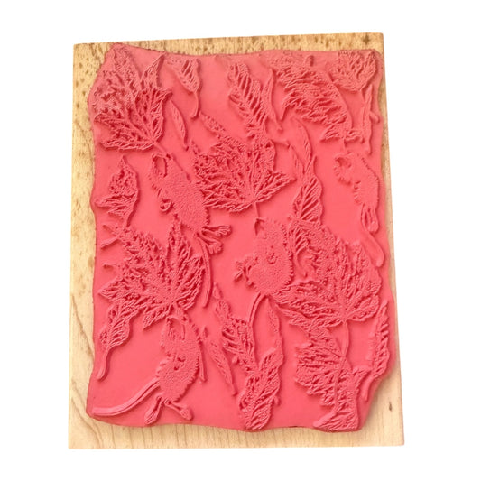 A pink rubber stamp with an embossed pattern of leaves and small mice, mounted on a light-colored wooden block against a plain white background.