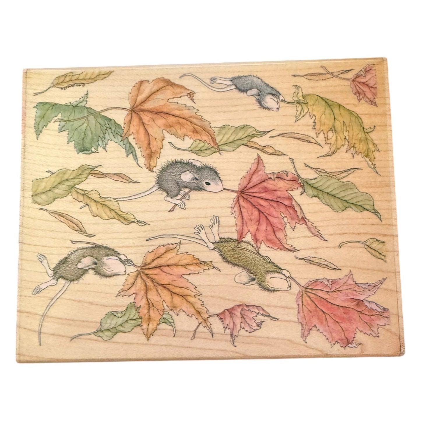 A square wooden block stamp  featuring a printed design of gray mice among autumn leaves in shades of green, orange, and red on a light wood grain background.