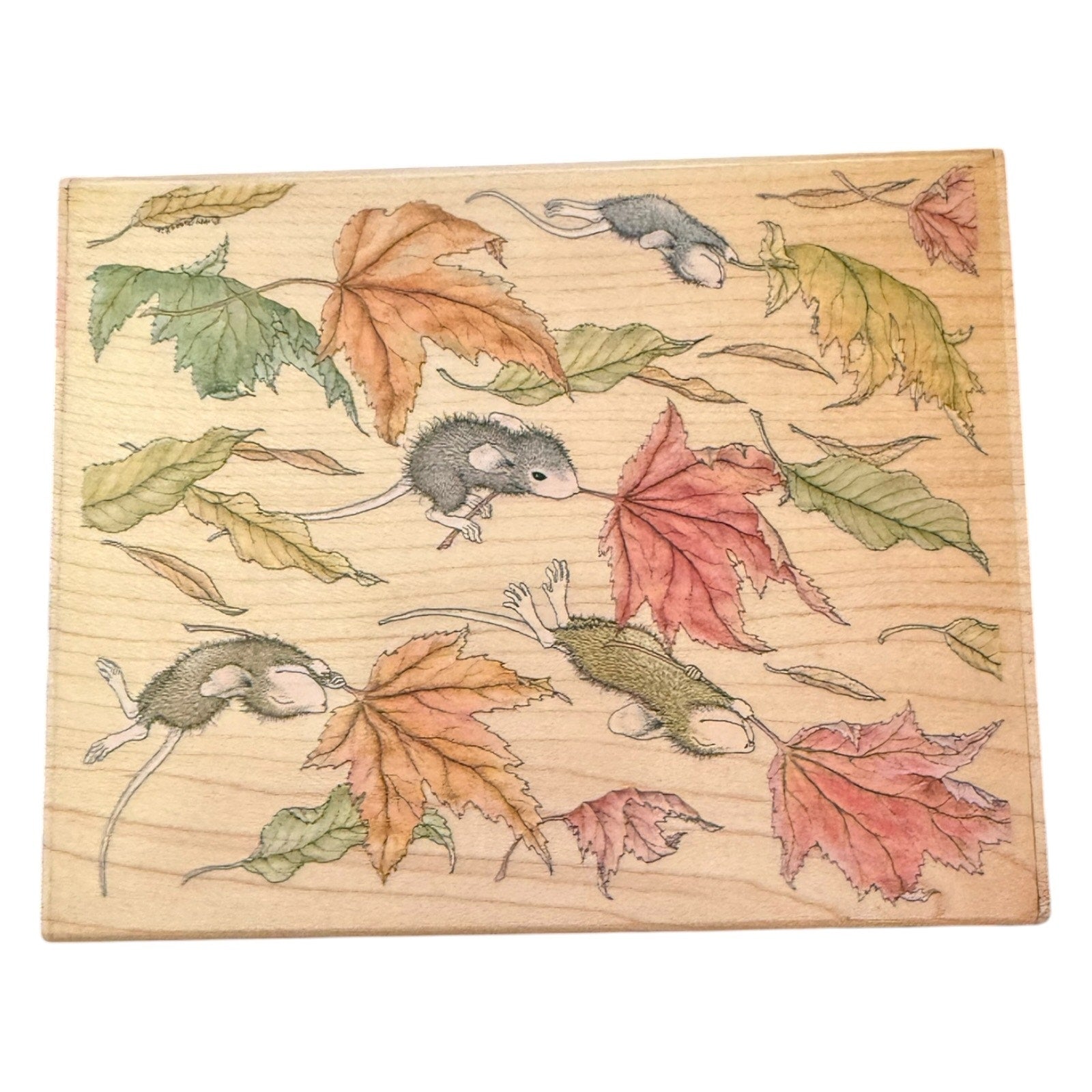 A square wooden block stamp  featuring a printed design of gray mice among autumn leaves in shades of green, orange, and red on a light wood grain background.
