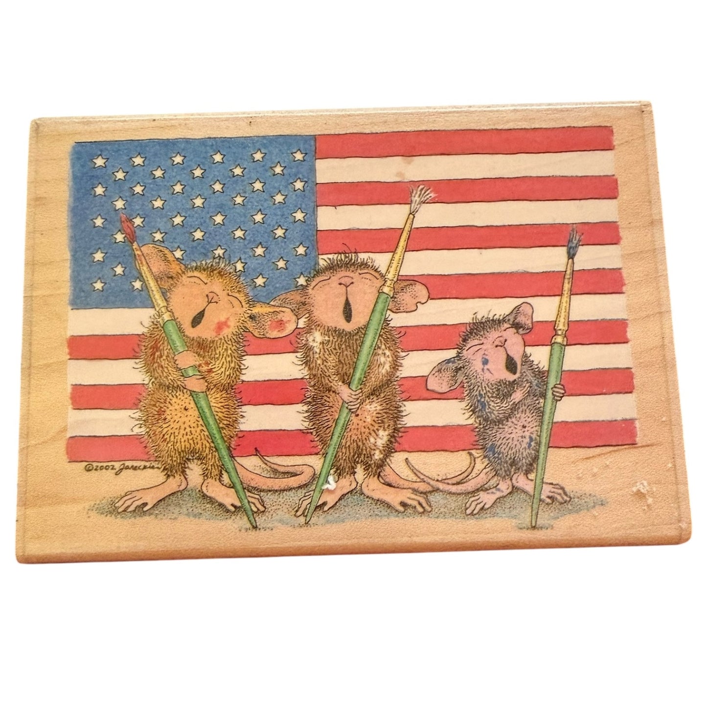 A square wooden stamp featuring three cartoon mice holding paintbrushes in front of an American flag. 