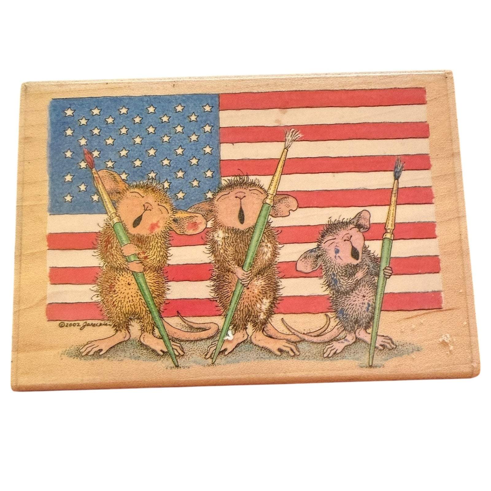 A square wooden stamp featuring three cartoon mice holding paintbrushes in front of an American flag. 