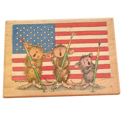 A square wooden stamp featuring three cartoon mice holding paintbrushes in front of an American flag. 