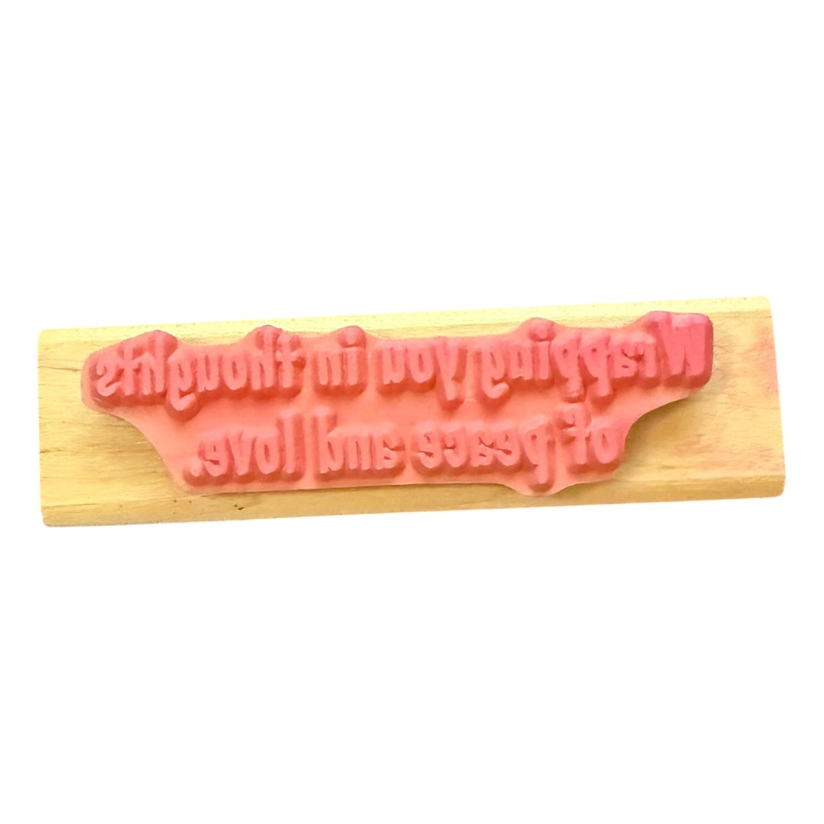 A pink rubber stamp with a decorative  text design, mounted on a light-colored wooden block, shown against a plain white background.