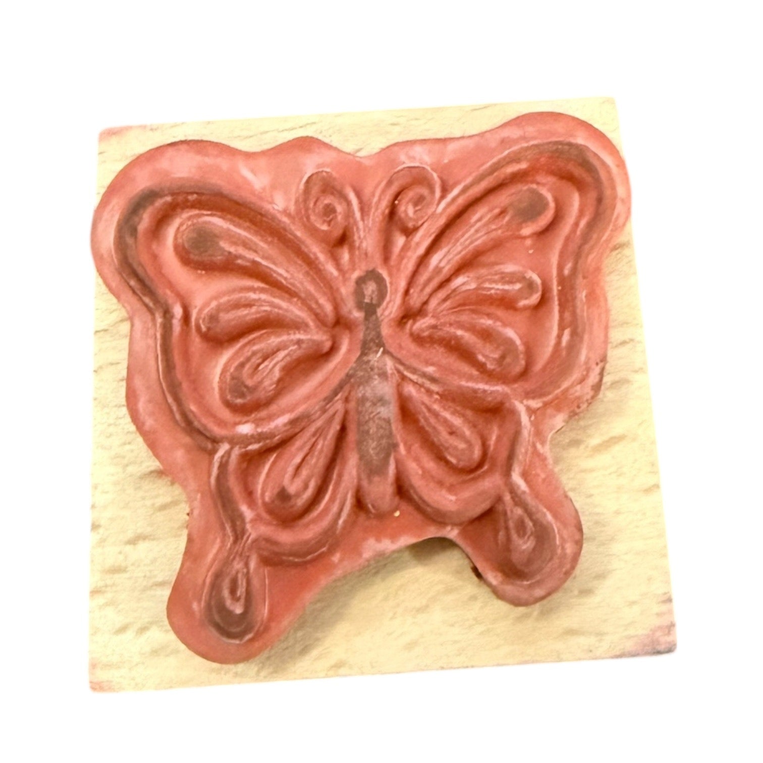 Butterfly-shaped stamp on a wooden block with a pinkish-brown design.