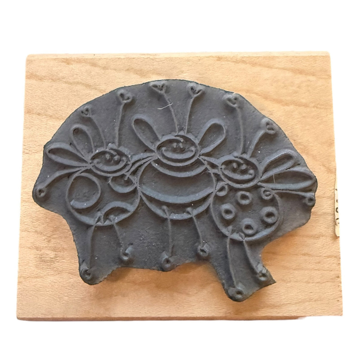 A dark gray stamp featuring three stylized bees, displayed on a light-colored wooden block against a white background.
