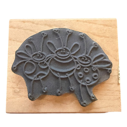 A dark gray stamp featuring three stylized bees, displayed on a light-colored wooden block against a white background.