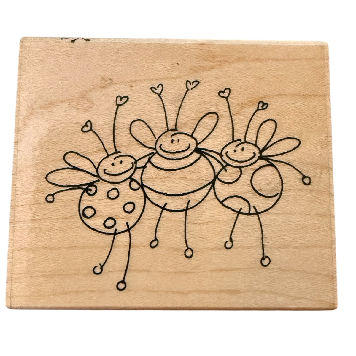A square wood stamp featuring a simple  drawing of three smiling bees on a light natural wood background, shown against a plain white backdrop.