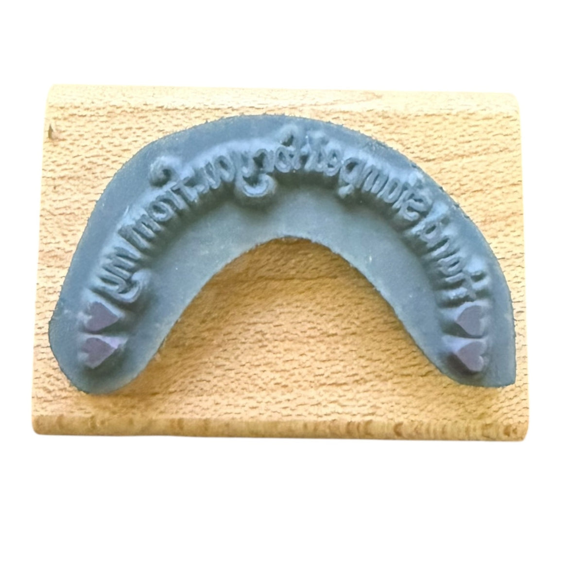 A gray rubber stamp, displayed on a light wood block against a white background.