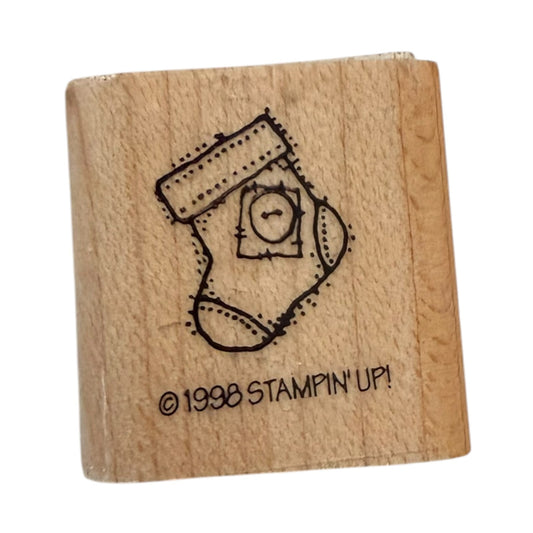 A wooden rubber stamp with a black  design of a Christmas stocking containing a small button, and the text '© 1998 STAMPIN' UP!' on the front, shown on a plain white background.