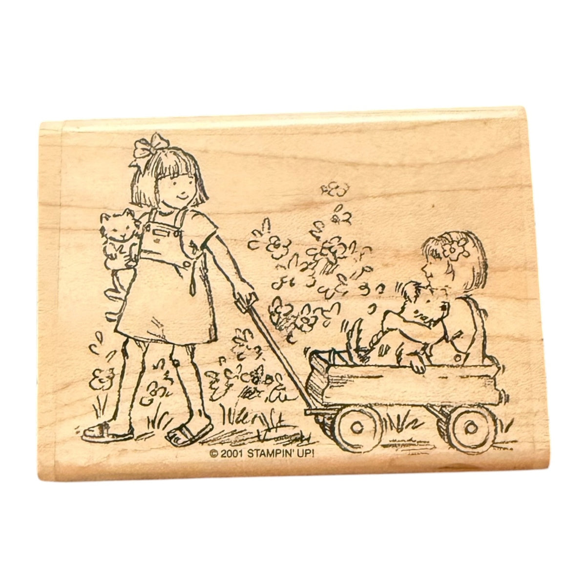 A wooden rubber stamp block featuring an illustration of a girl pulling a wagon with a child & dog sitting inside, plus a small cat, on a plain white background.