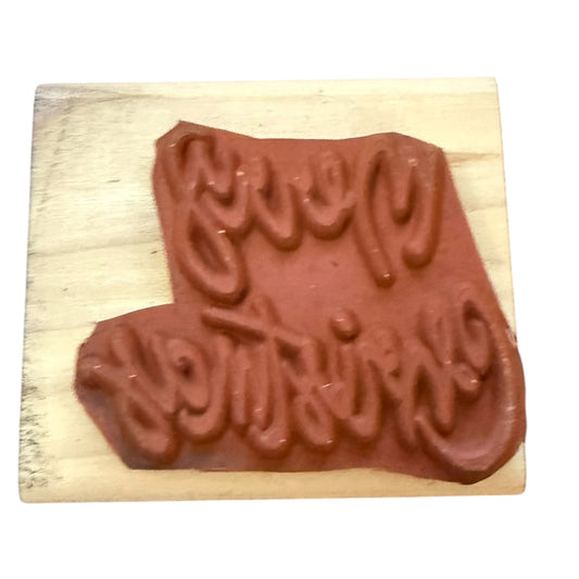A wooden rubber stamp featuring the phrase 'Merry Christmas' in raised cursive lettering, shown on a plain white background.