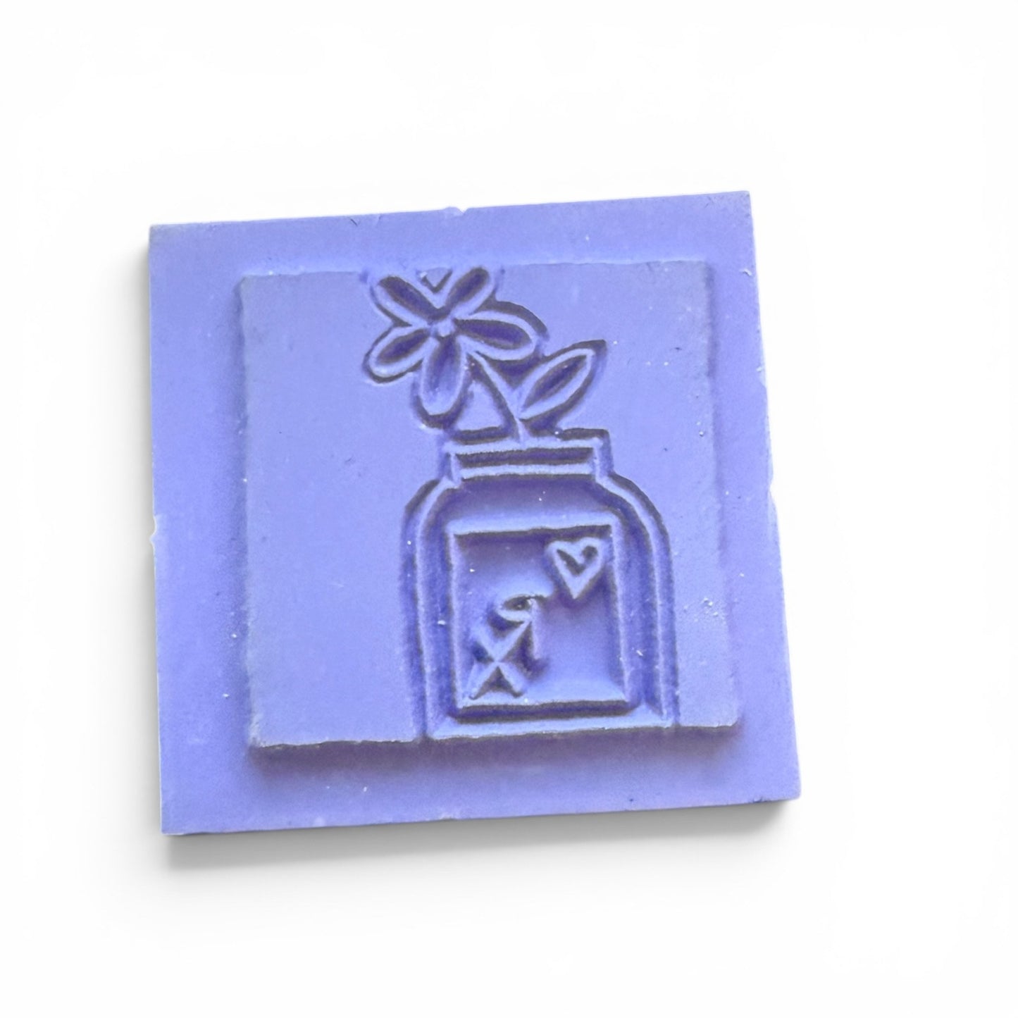 square stamp with a design of a bottle and flower on a white background