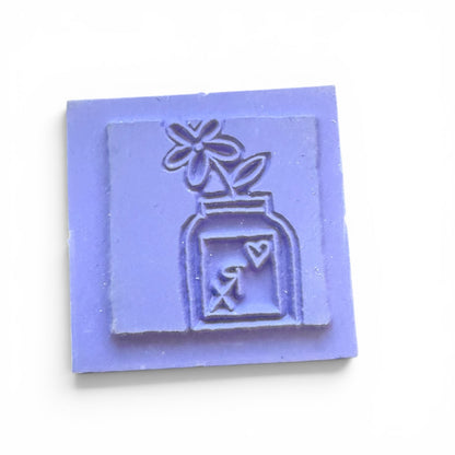 square stamp with a design of a bottle and flower on a white background