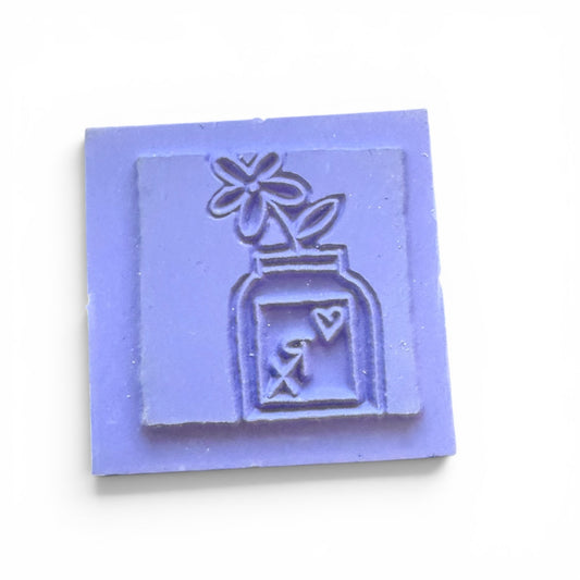 square stamp with a design of a bottle and flower on a white background