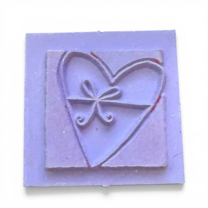 Purple rubber stamp with heart and bow design on a white background