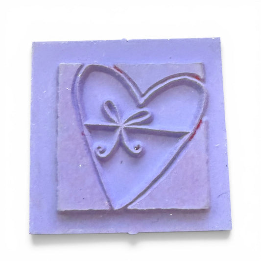 Purple rubber stamp with heart and bow design on a white background
