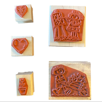 Five wooden rubber stamps shown on a white background, including heart and garden-themed embossed designs in reddish-brown rubber.