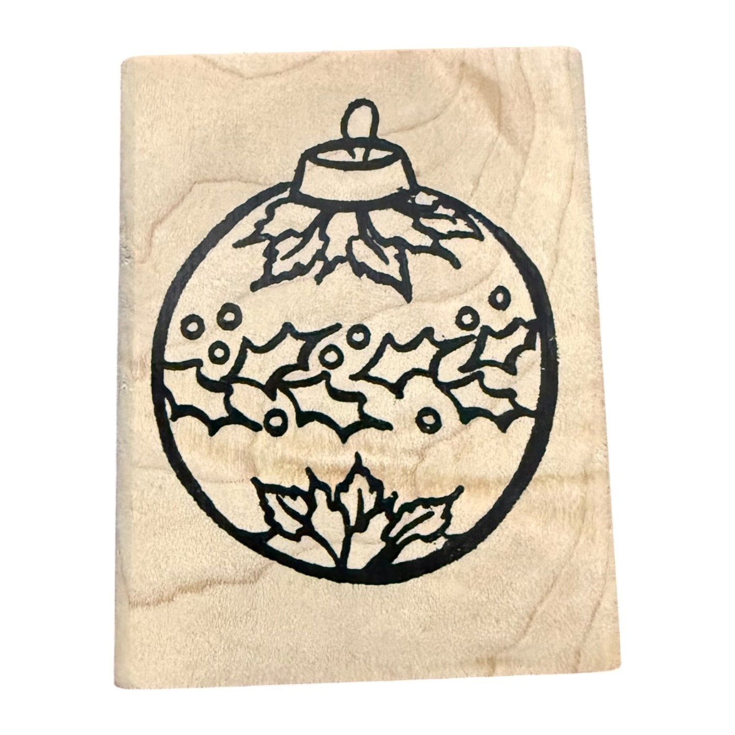 A wooden rubber stamp featuring a black line-art design of a Christmas ornament decorated with holly leaves and berries, shown on a plain white background.