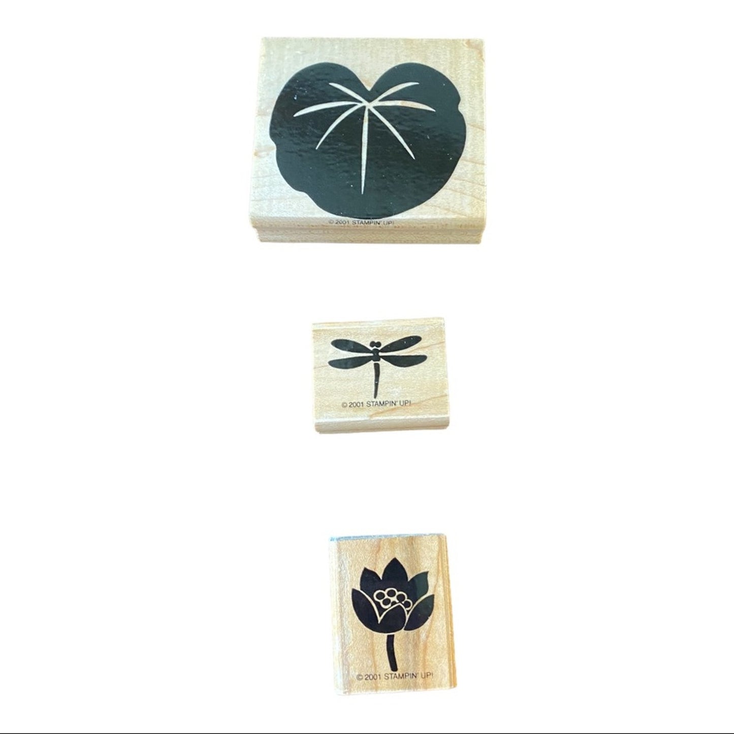 Three wooden rubber stamps shown vertically on a white background, featuring a lily  pad, a dragonfly, and a lotus flower with small white details.