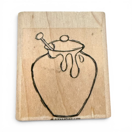 Wooden block with a black line drawing of a honey jar and spoon on a white background