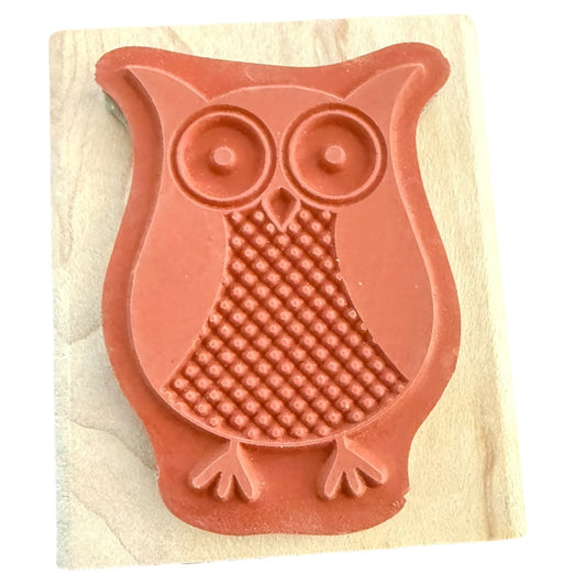 An owl-shaped rubber stamp made of terracotta-colored material, mounted on a light-colored wooden block against a white background.