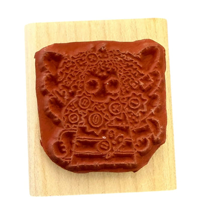 A square wooden rubber stamp , displayed on a light wood block against a white background.