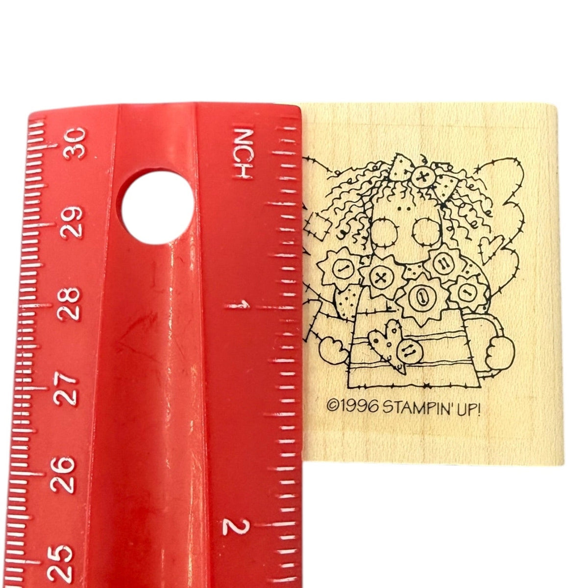 A wooden rubber stamp shown next to a red plastic ruler for scale on a white background.