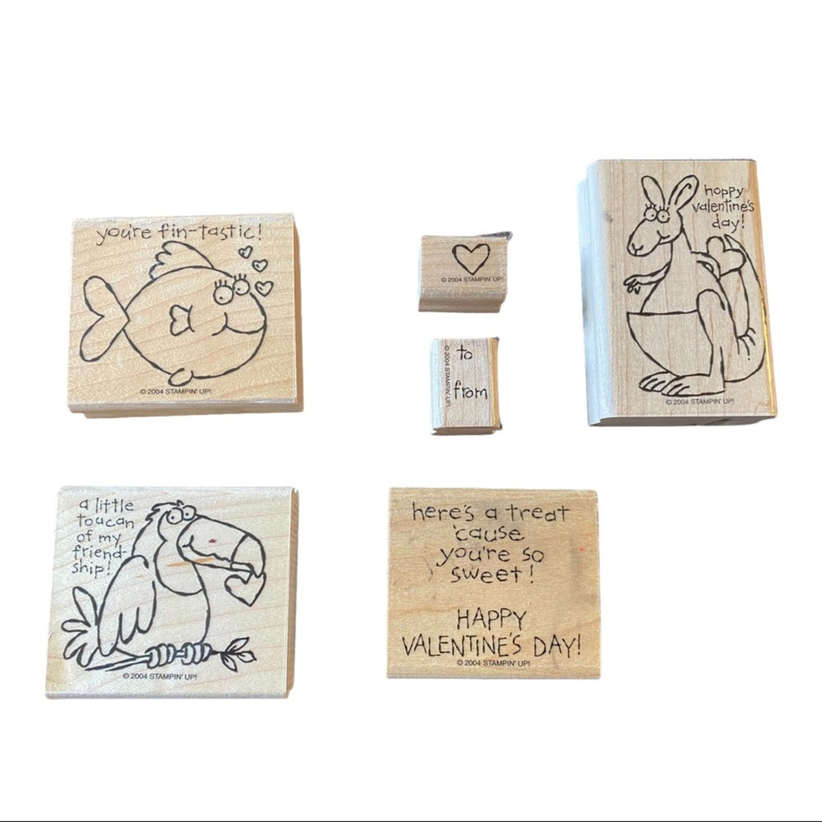 Six wooden rubber stamps with Valentine's Day themed illustrations and text, arranged on a plain white background. The designs include a fish, a kangaroo, a toucan, and text messages such as 'you're fin-Tastic!', 'happy Valentine's Day!', and 'here's a treat you're so sweet!'.