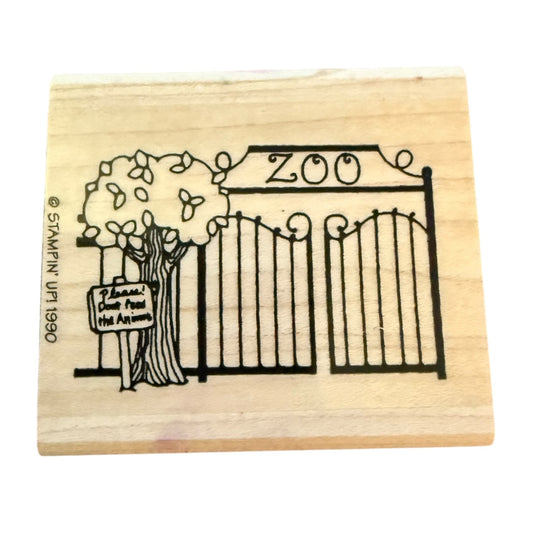 Rubber stamp with a design of a zoo gate and tree on a wooden block.