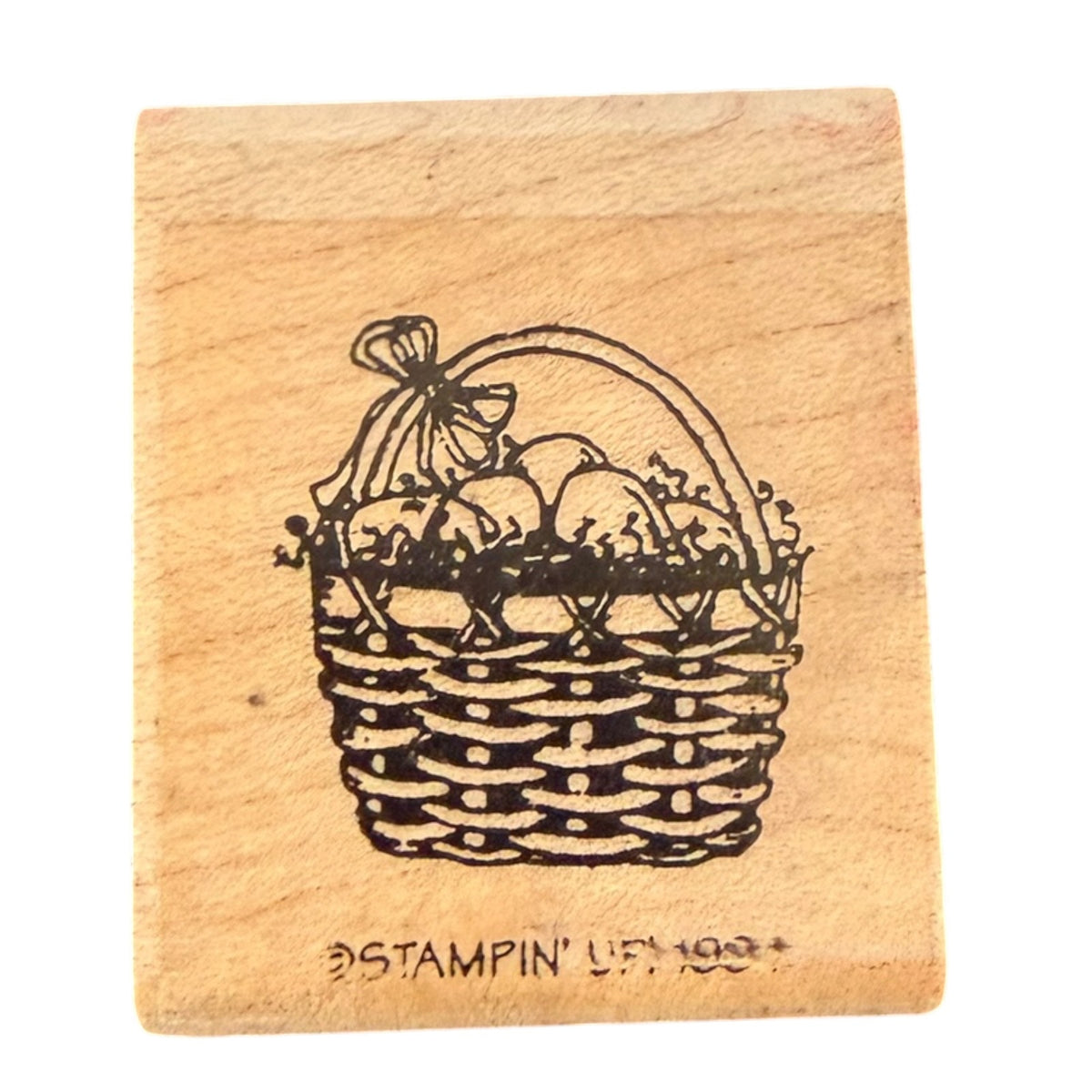A square wooden rubber stamp block featuring a black illustration of an Easter basket filled with eggs and a bow, with the text 'STAMPIN' UP 1994' debossed at the bottom, shown on a plain white background.