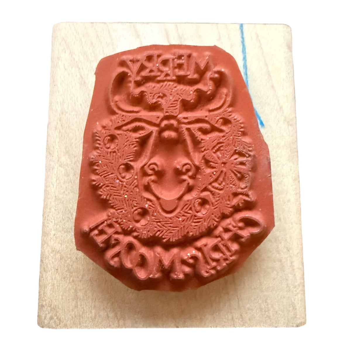 A terracotta-colored rubber stamp featuring a festive holiday design with a reindeer resting on a light-colored wooden block.