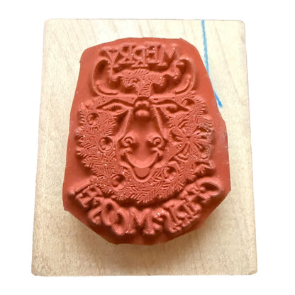 A terracotta-colored rubber stamp featuring a festive holiday design with a reindeer resting on a light-colored wooden block.