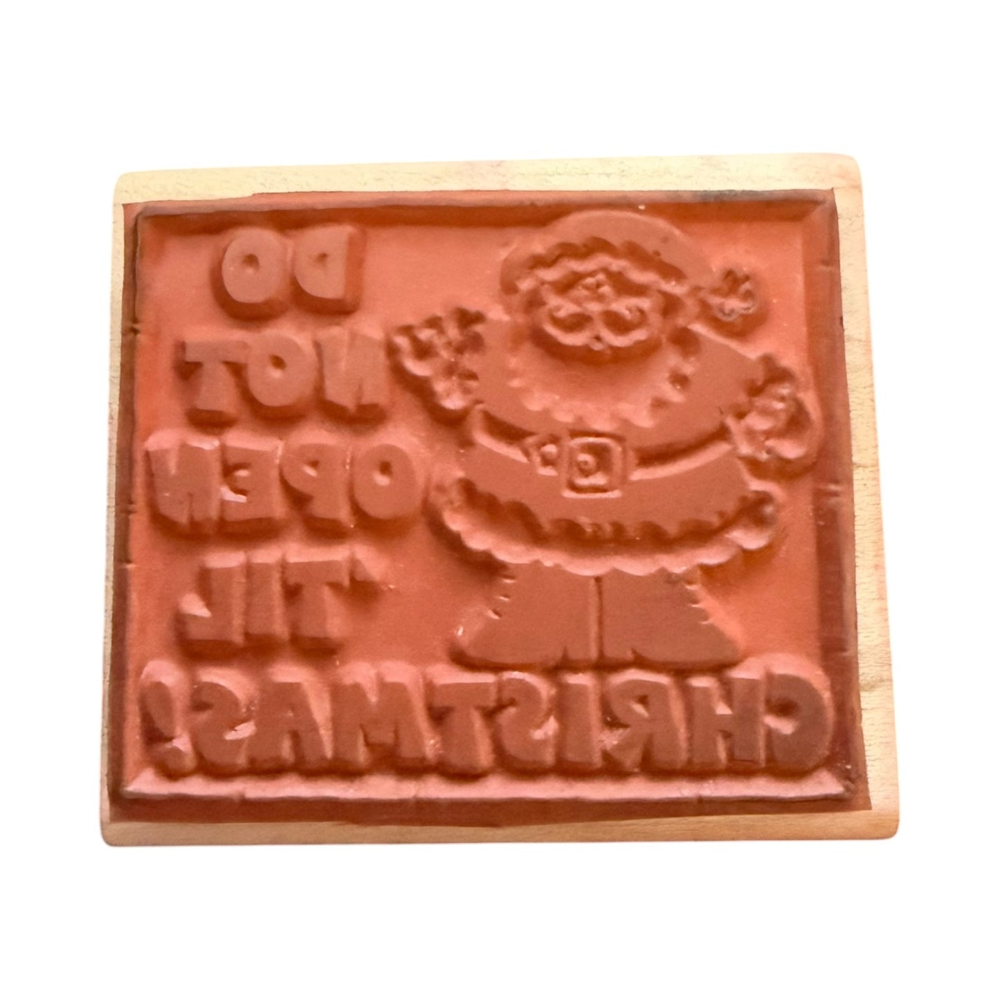 A wooden Christmas-themed rubber stamp featuring a raised Santa Claus figure and the text 'DO NOT OPEN TIL CHRISTMAS' in relief, shown on a plain white background.