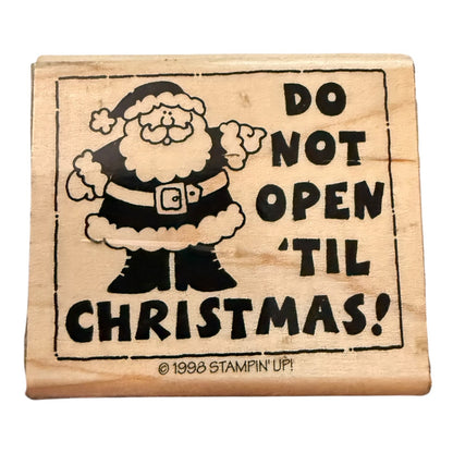 A wooden rubber stamp featuring a black-and-white illustration of Santa Claus and the text 'DO NOT OPEN 'TIL CHRISTMAS!' on a light wood block, with a small '© 1998 STAMPIN' UP!' copyright line at the bottom.