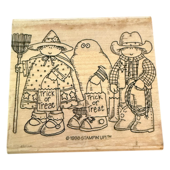 Wooden stamp with illustrations of a witch, ghost, and cowboy holding Halloween-themed items.