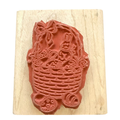 A rubber stamp featuring a bunny in a basket with floral details, mounted on a light-colored wooden block against a white background.