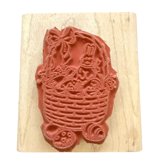 A rubber stamp featuring a bunny in a basket with floral details, mounted on a light-colored wooden block against a white background.