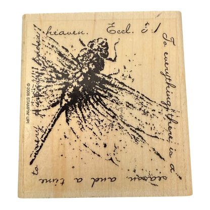 A square wooden stamp block featuring a black ink illustration of a dragonfly, surrounded by handwritten-style religious and inspirational text on a light wood background.