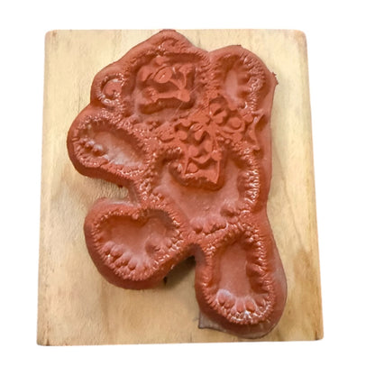 A terracotta-colored rubber stamp featuring a stylized bear design , mounted on a light-colored wooden block against a white background.