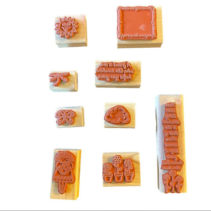 A set of nine wooden rubber stamp blocks with various decorative and text-based designs, arranged on a plain white background.