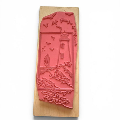 Decorative rubber stamp with a lighthouse design on a wooden block.