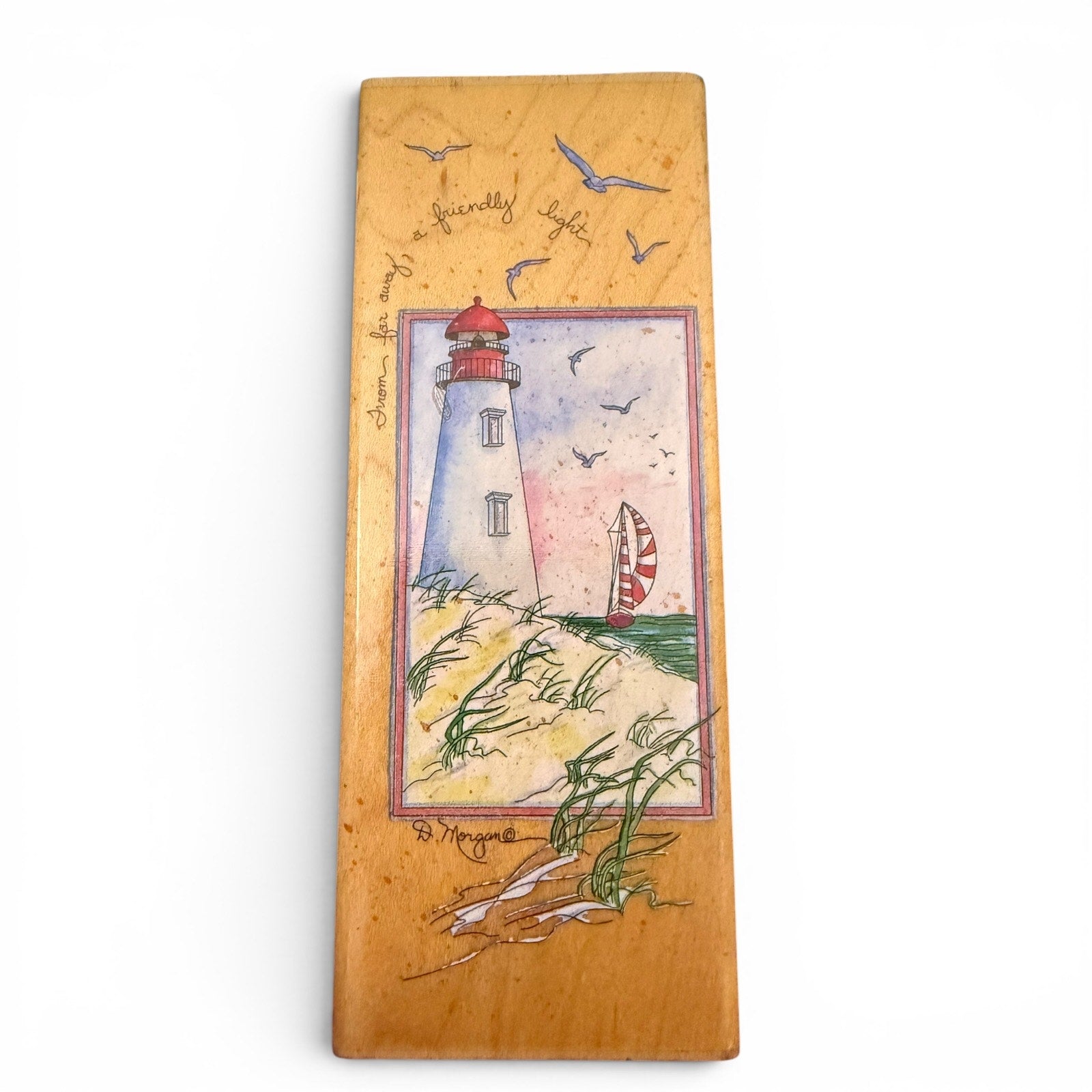 Wooden stamp with a lighthouse illustration and text on a white background