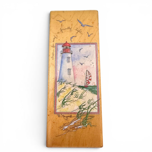 Wooden stamp with a lighthouse illustration and text on a white background