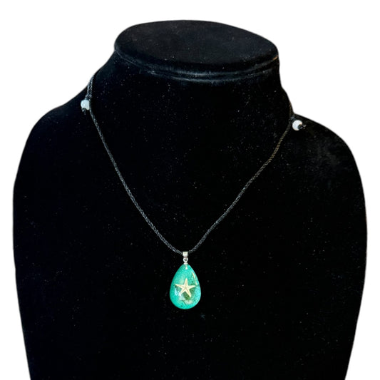 Necklace with a green teardrop pendant  with a starfish on a black mannequin bust.